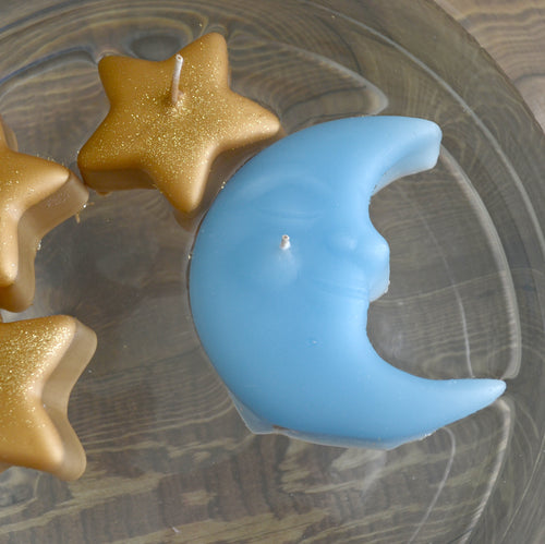 sky blue crescent moon candle floating in a bowl with three small golden star shaped candles 