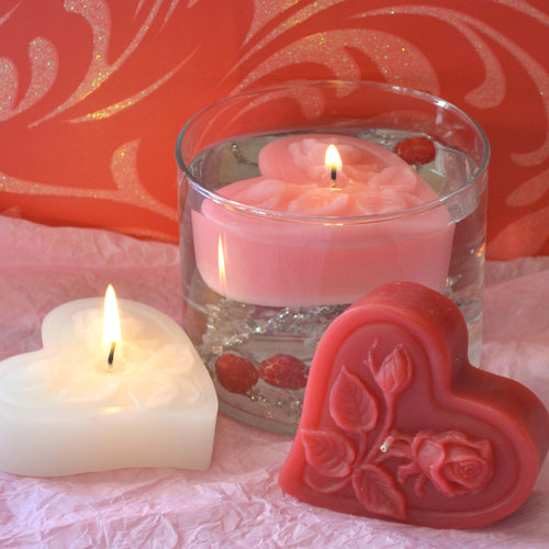 three floating heart candles with roses on top in pink, white and red floating in a clear glass cylinder for valentines day centerpieces