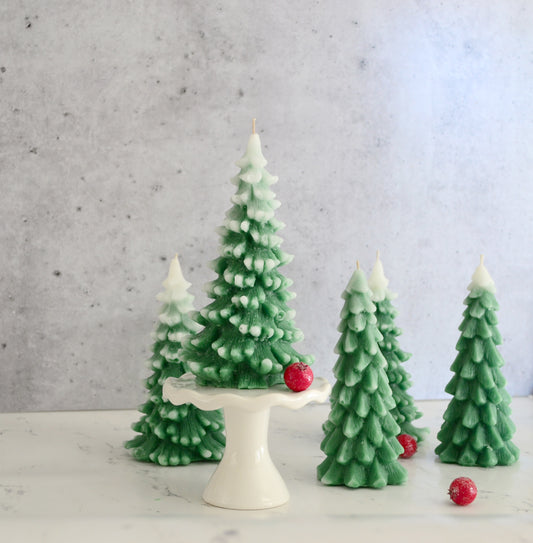 Centered snow topped green wax Christmas tree on white pedestal. Several tree shaped candle surrounded by red berries