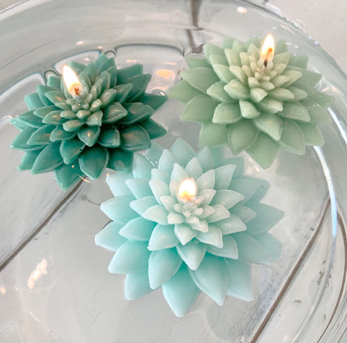 Three succulent shaped floating candles of varying green color floating in a wedding centerpiece. 