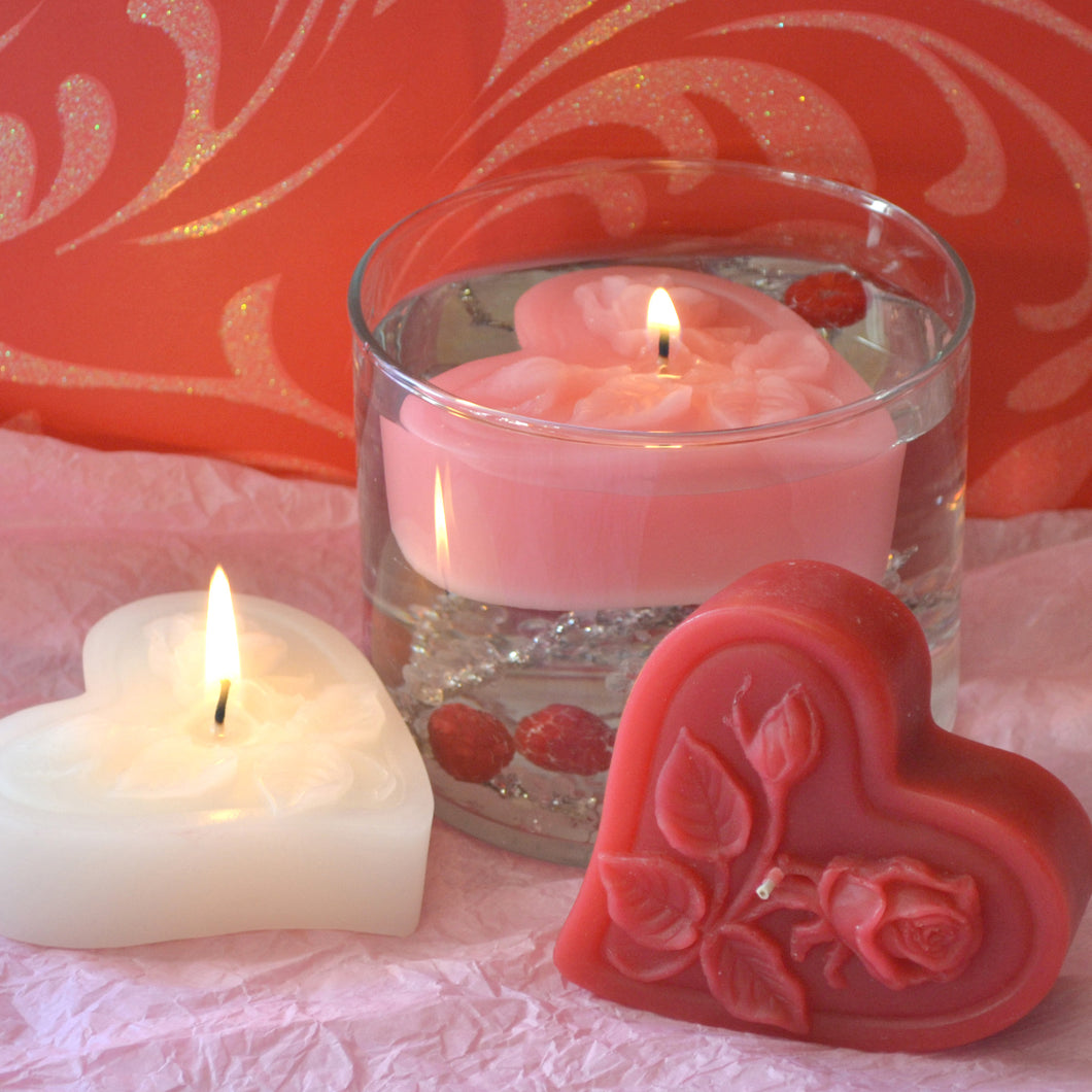 three floating heart candles with roses on top in pink, white and red floating in a clear glass cylinder for valentines day centerpieces
