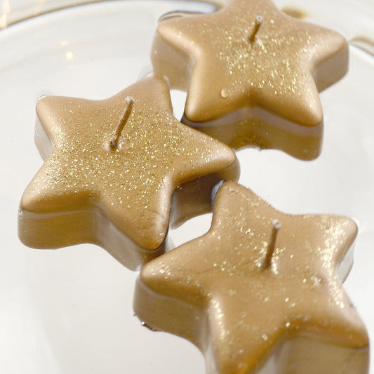 Three golden star shaped candles floating in  bowl of water